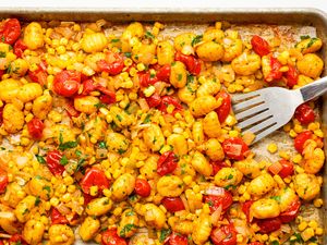 A close-up of cooked gnocchi with cherry tomatoes and corn on a sheet pan with a fork