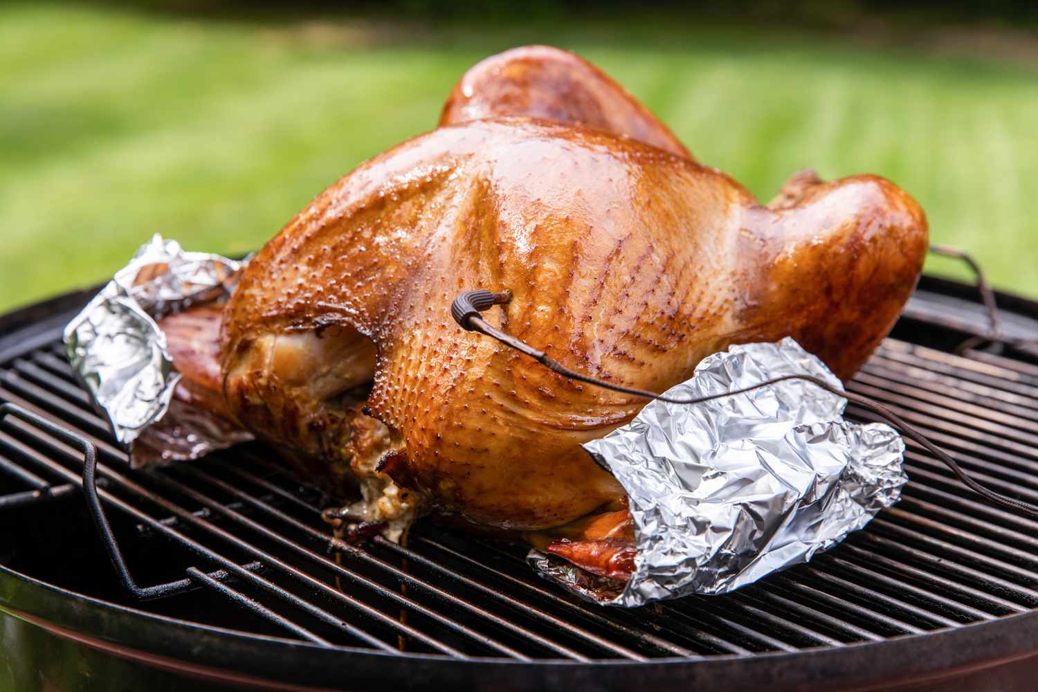 Covering the turkey wings with foil on a smoker to make citrus-brined smoked turkey.