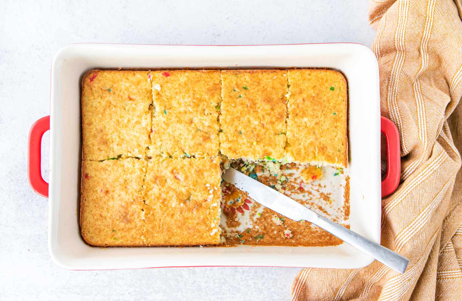 Funfetti Cake in a Baking Dish Cut into Pieces Using a Knife with Some of the Pieces Removed
