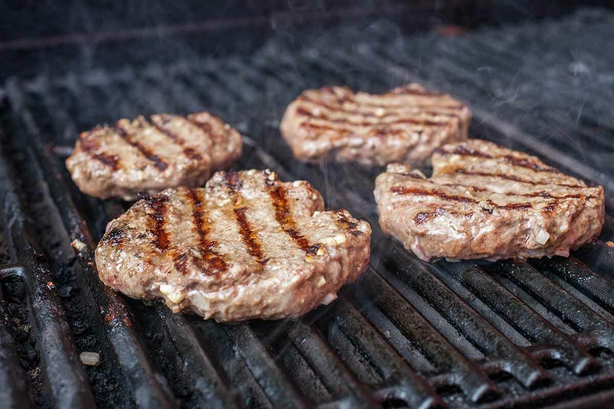 Four burger patties with grill marks cooking on a grill