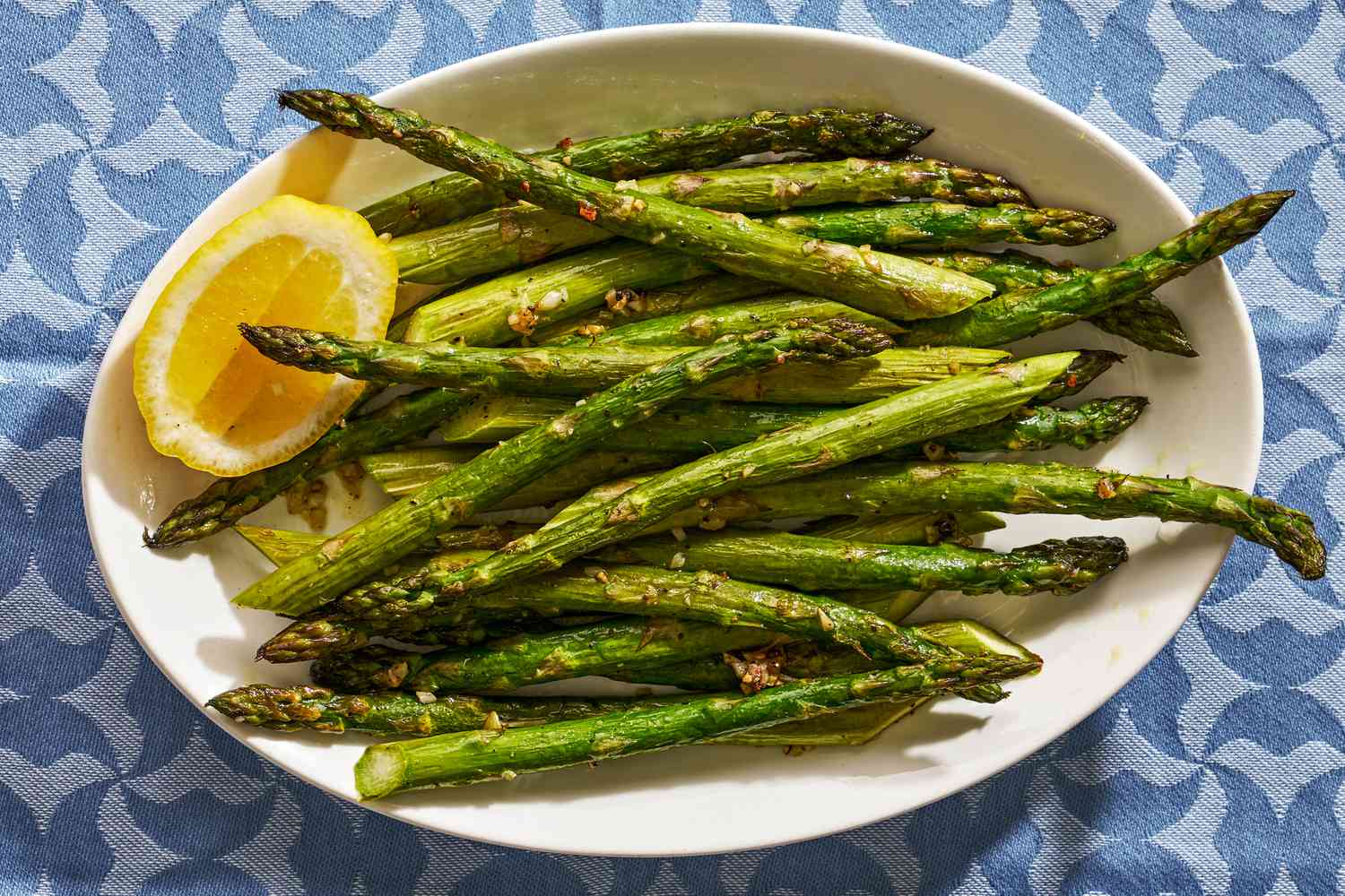 A white serving plate with cooked asparagus and a lemon wedge for garnish