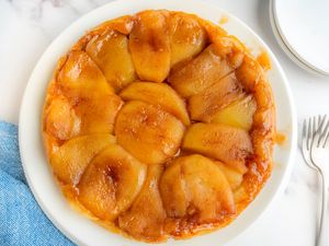 A tarte tatin placed on a white plate a dessert consisting of caramelized fruit arranged over a pastry base