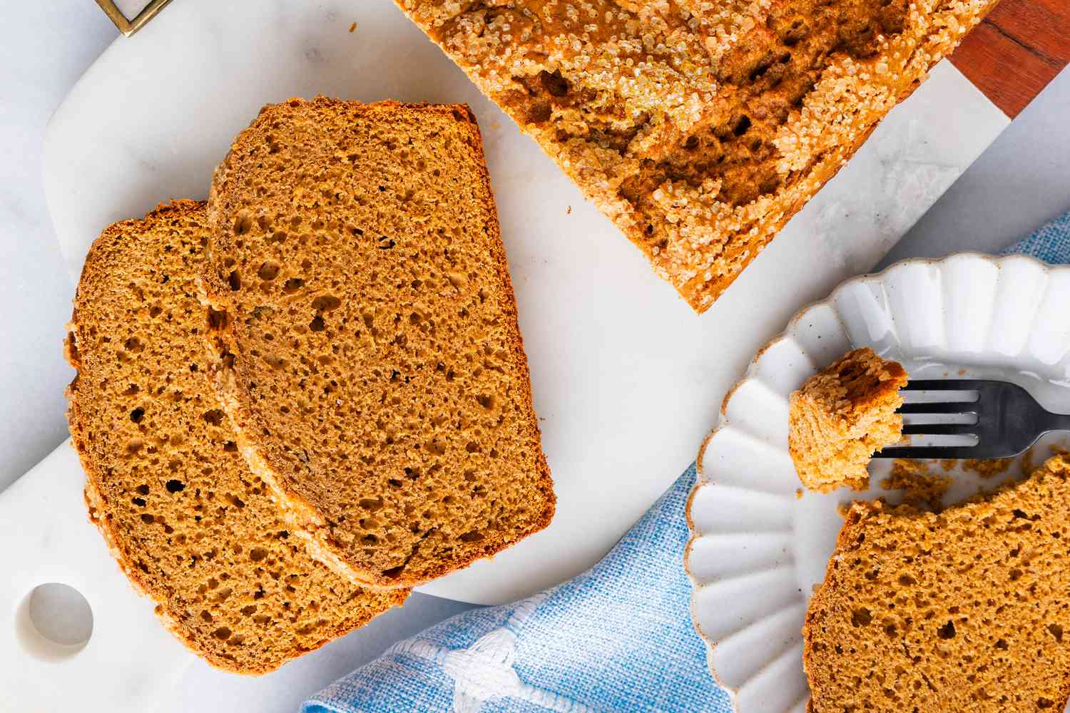 Overhead view of a loaf of pumpkin bread on a marble cutting board with two slices in front and one on a plate with a fork to the side