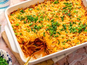 A baked casserole topped with shredded cheese and chopped green onions one serving removed with a spoon in the dish