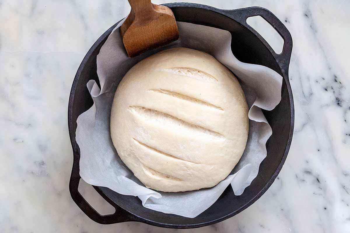 Dutch Oven Bread dough with slits on the top and a piece of parchment underneath.