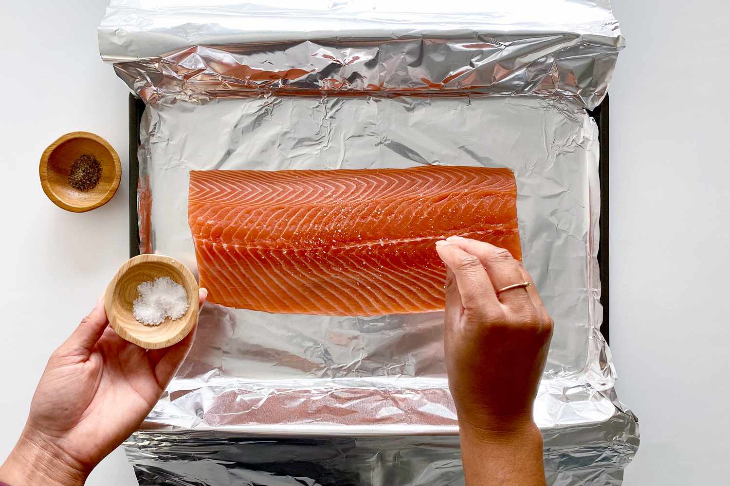 Seasoning salmon on a foil lined baking sheet with salt and peper