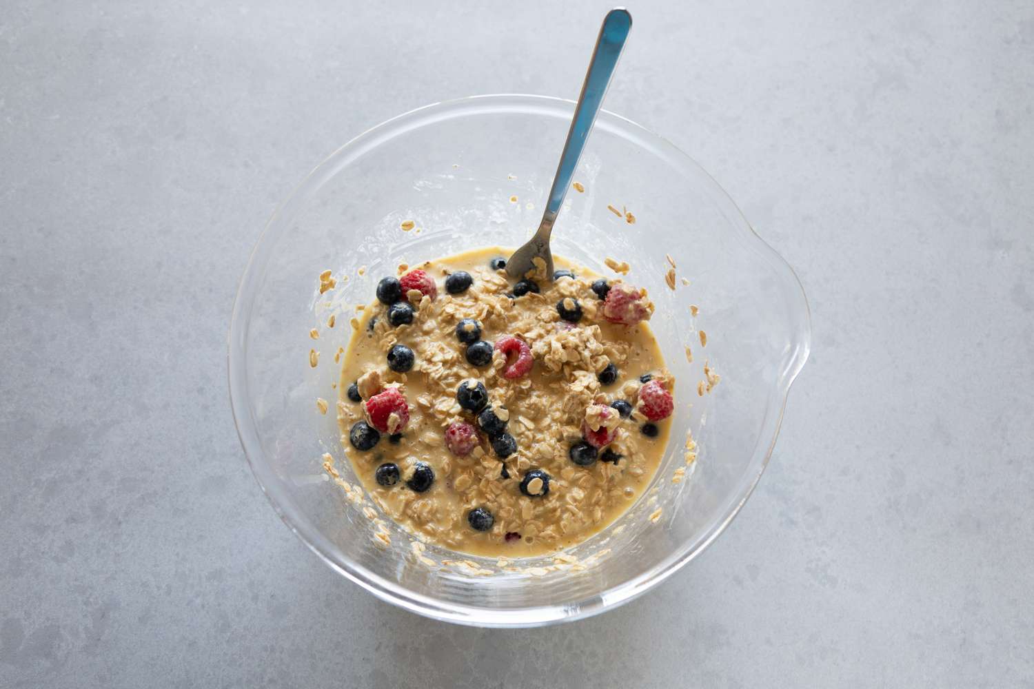 Berries mixed into oatmeal in a glass bowl to make Mixed Berry Baked Oatmeal.