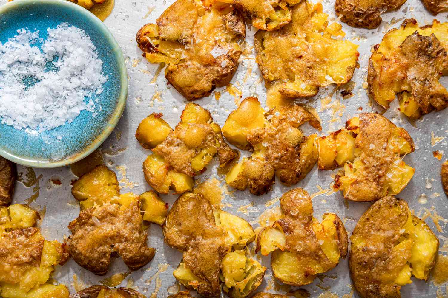 Crash hot potatoes and a small saucer with flaky salt on a baking sheet