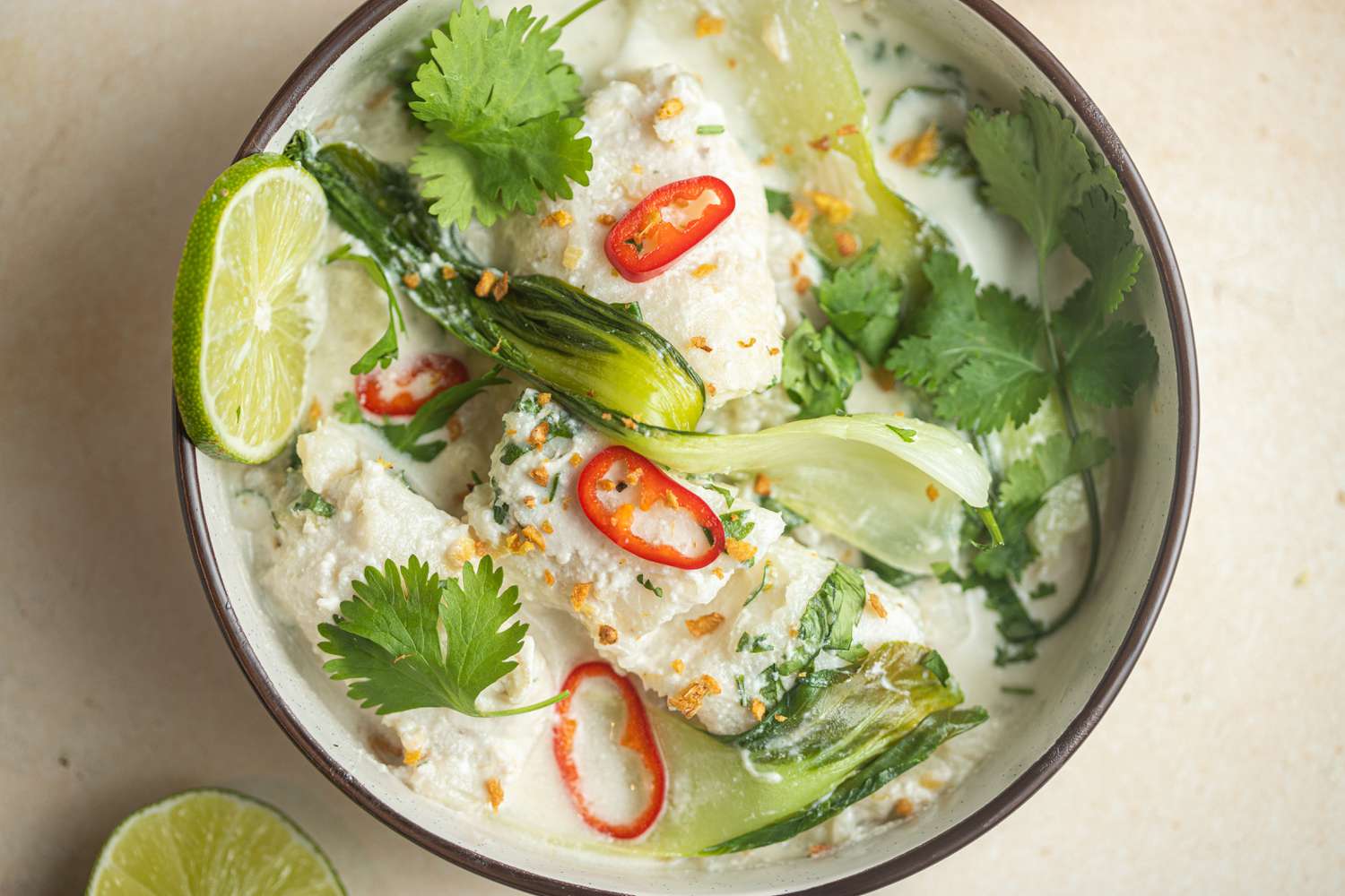 Overhead view of a bowl of Coconut poached fish with bok choy, ginger, and lime.