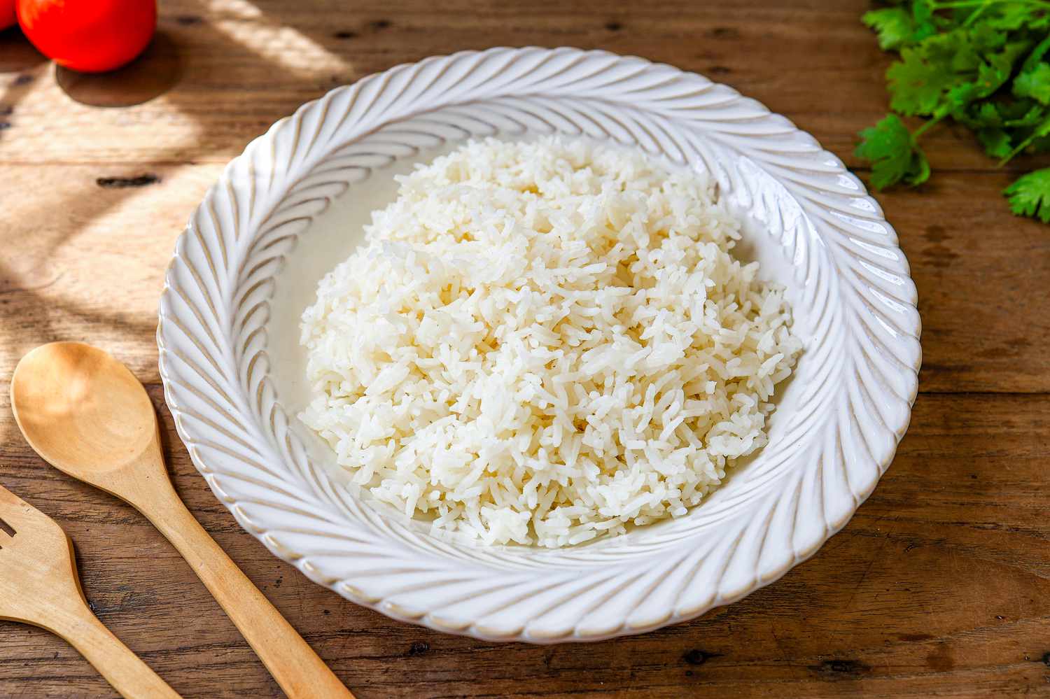 Cooked white rice or steamed rice in a white bowl on wooden background next to two wooden serving utensils