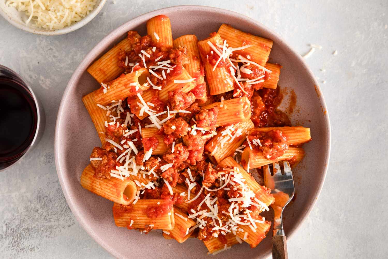 Rigatoni pasta topped with sausage tomato sauce and shredded cheese served on a plate with a fork