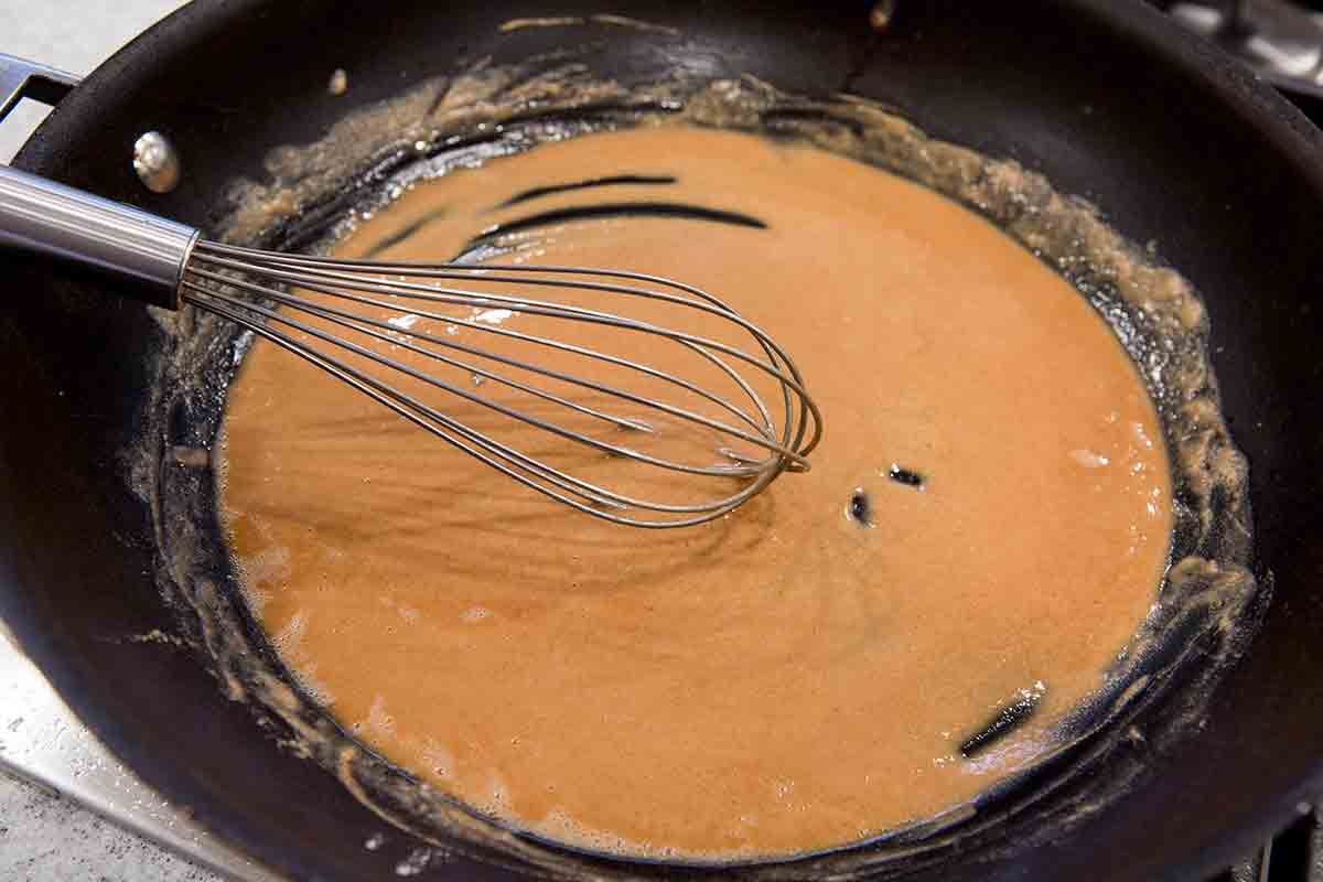 A Swedish meatball sauce browning and being whisked on a pan