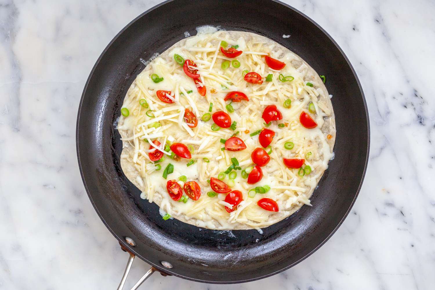 Tomatoes and cheese on a skillet to make a quesadilla recipe.