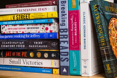 A stack of cookbooks arranged on a shelf showcasing various titles by different authors
