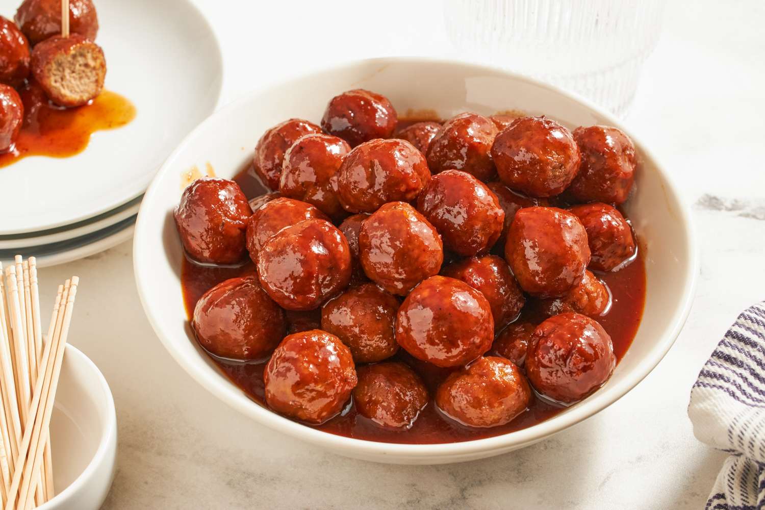 Bowl of cocktail meatballs in sauce on a table with toothpicks nearby