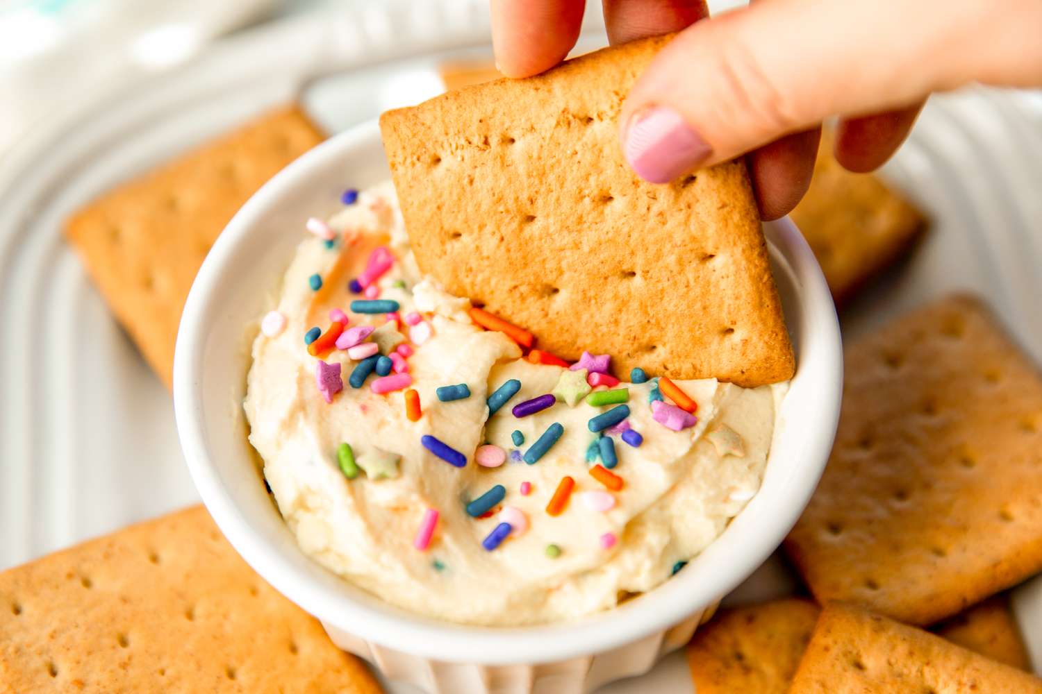 Bowl of yogurt frosting topped with sprinkles, surrounded by graham crackers
