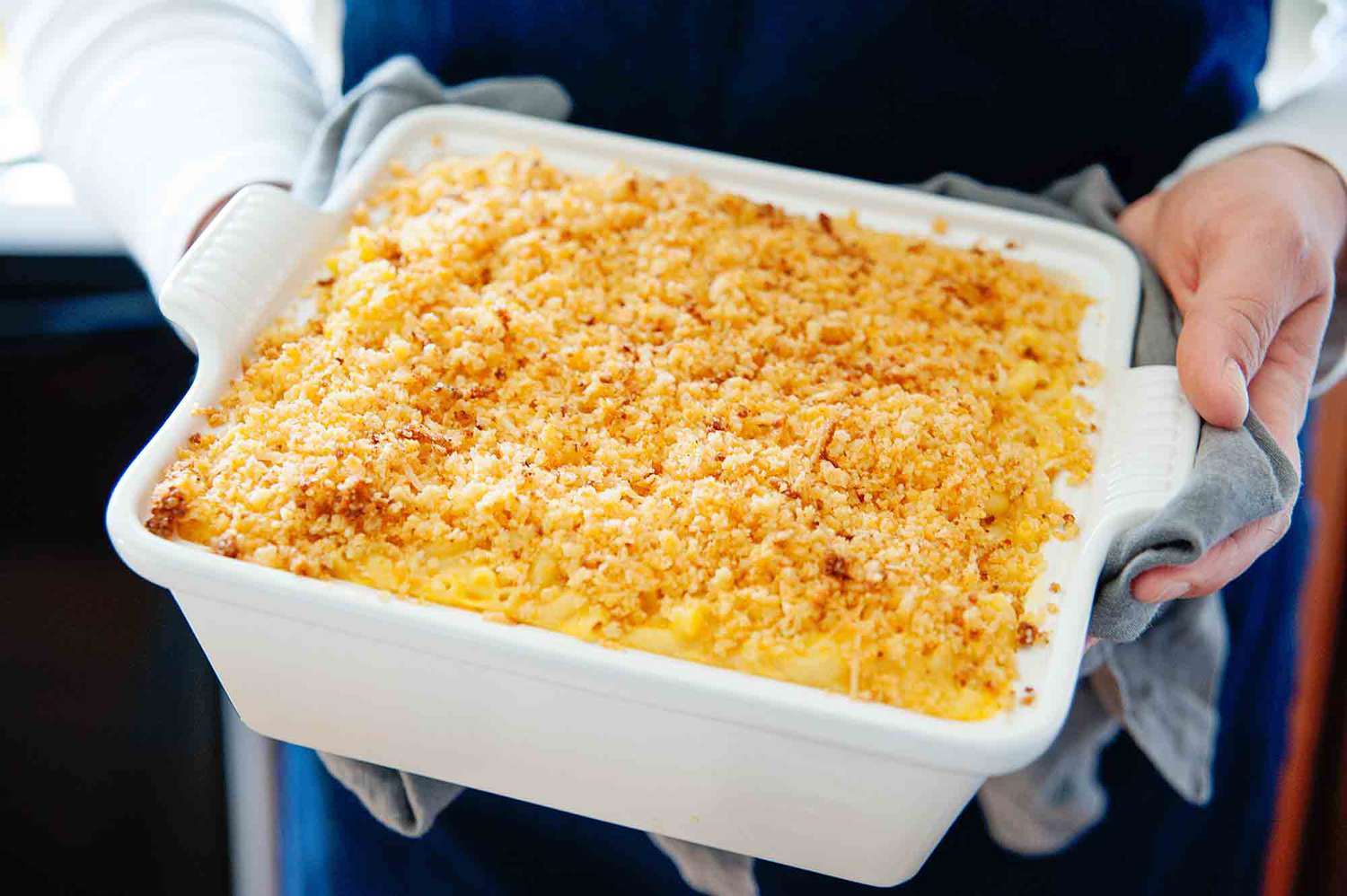 Kraft mac and cheese - woman's hands holding a white casserole dish filled with baked mac and cheese