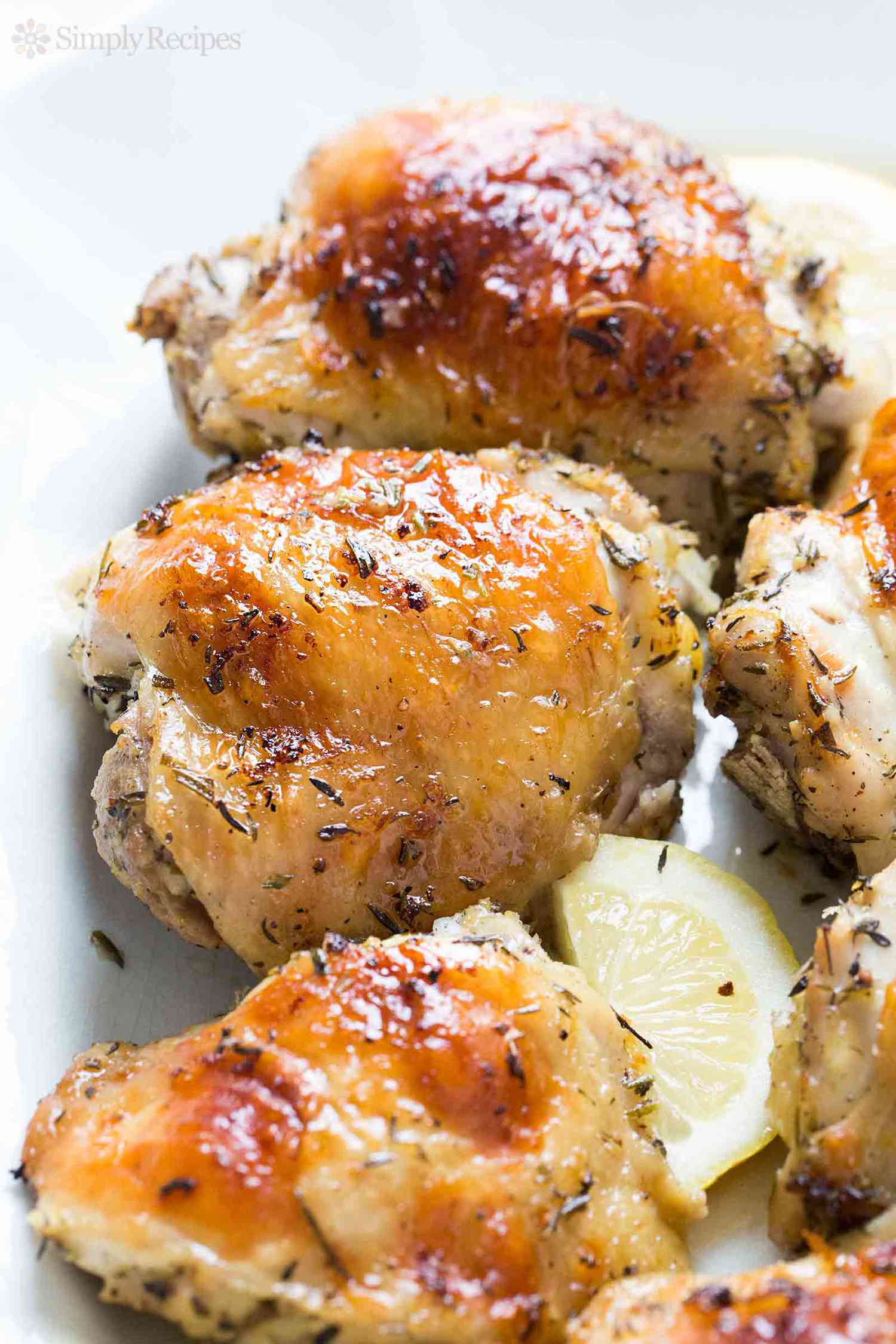 Some lemon chicken resting on a platter with lemon slices