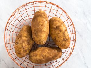 Four raw potatoes in a wire basket on a marble kitchen counter