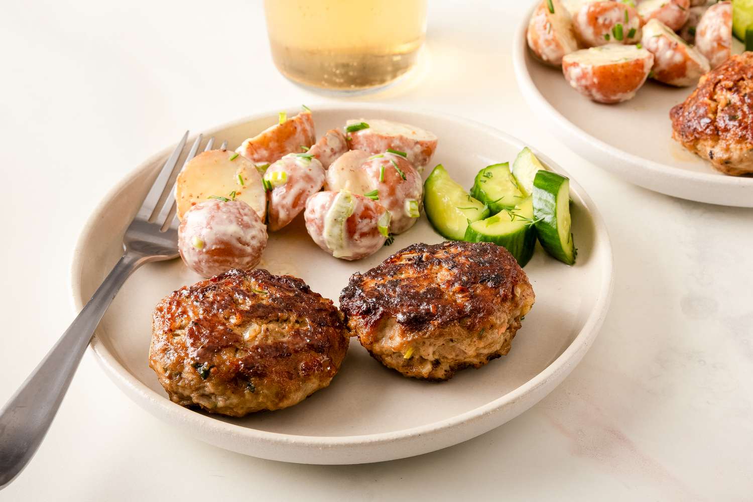 Frikadellen with a side of potato salad and cucumber slices on a plate
