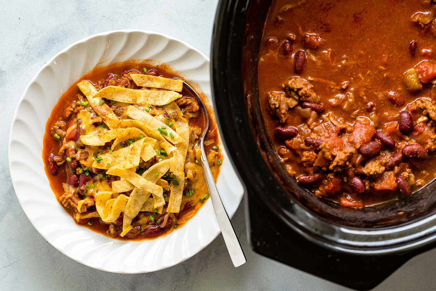 A bowl of chili with tortilla strips and a slow cooker filled with chili beside it