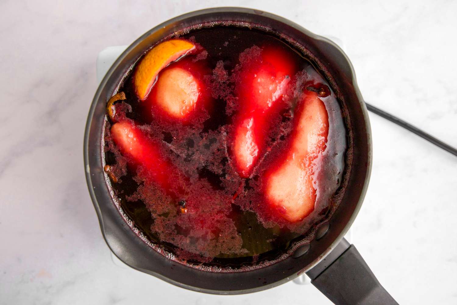 Pears poaching in red wine sauce in pot.