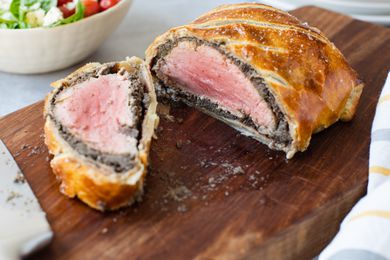 Beef Wellington Sliced in Half on a Cutting Board Next to a Bowl of Side Salad