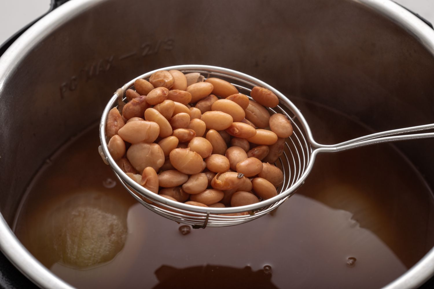Straining refried beans out of a pressure cooker.