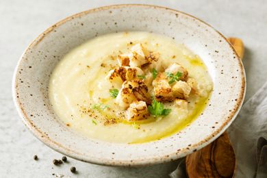 A bowl of creamy soup topped with roasted cauliflower and garnished with herbs