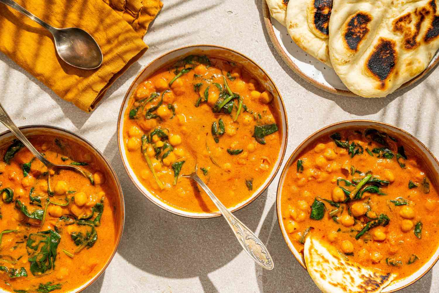 3 bowls of Easy Chickpea Curry with spoons, naan on the side