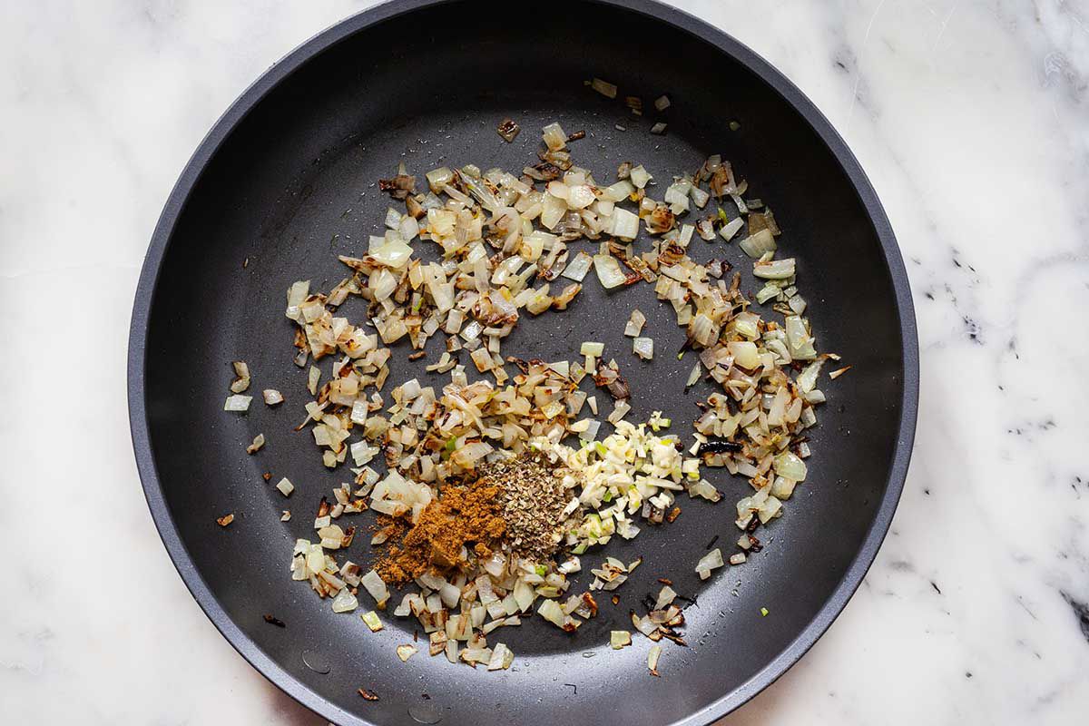 Diced onion and spices in a saute pan on a marble background.
