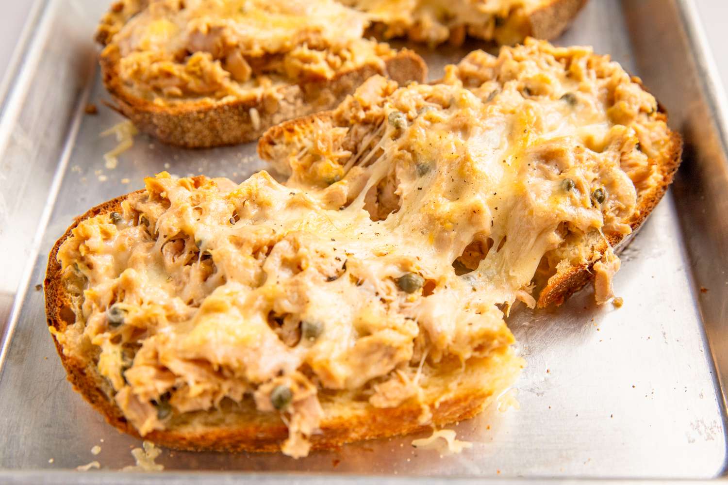 Toasted bread topped with melted cheese and tuna mixture on a baking tray