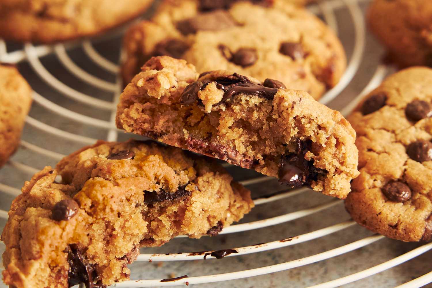 Chocolate chip cookies on a cooling rack one split open to show the interior texture