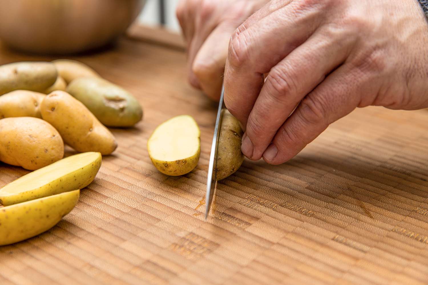 Fingerling Potatoes Cut in Half on a Cutting Board Using a Knife, and on the Cutting Board, More Fingerling Potatoes