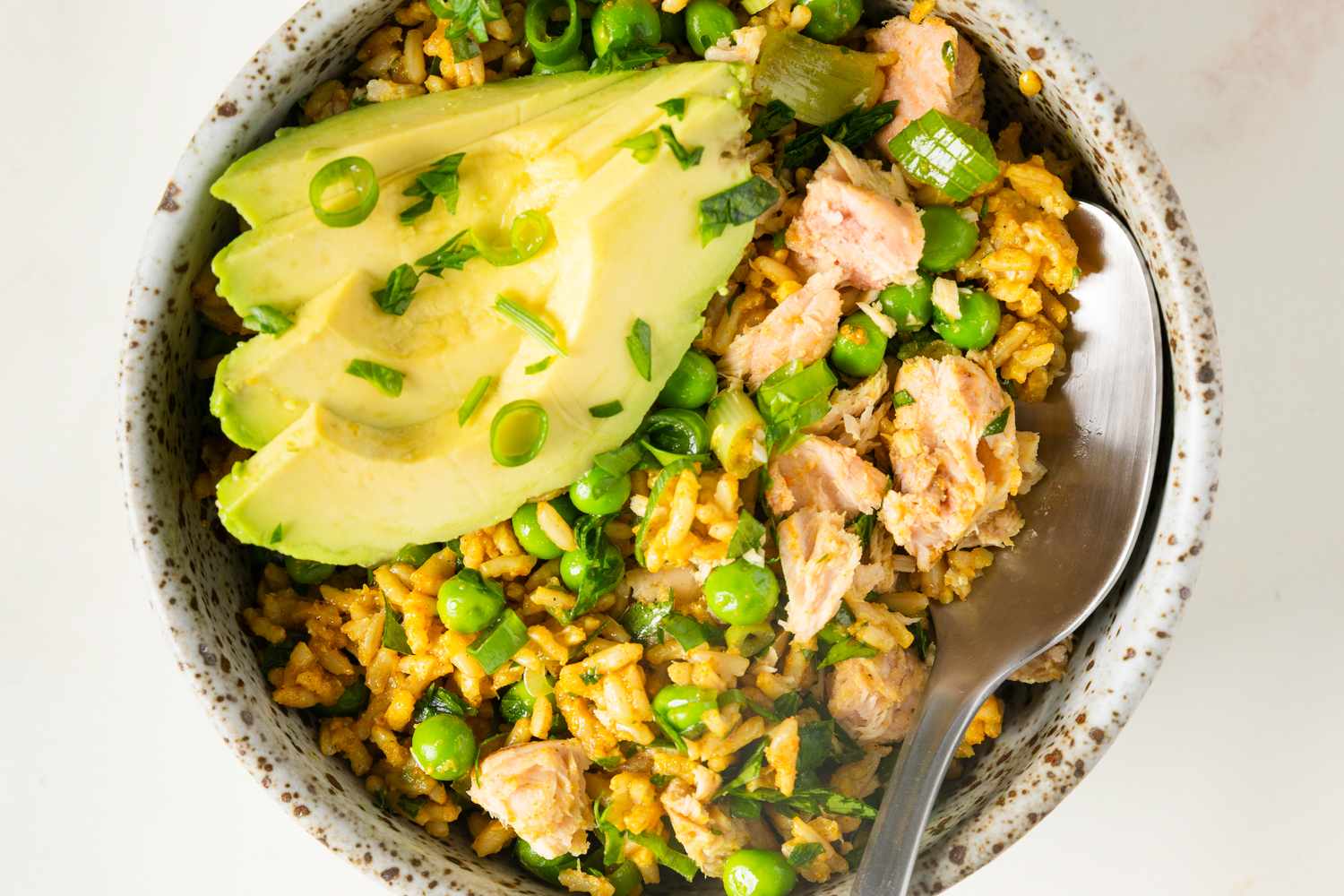 Rice dish topped with salmon flakes peas green onions and sliced avocado served in a bowl with a spoon