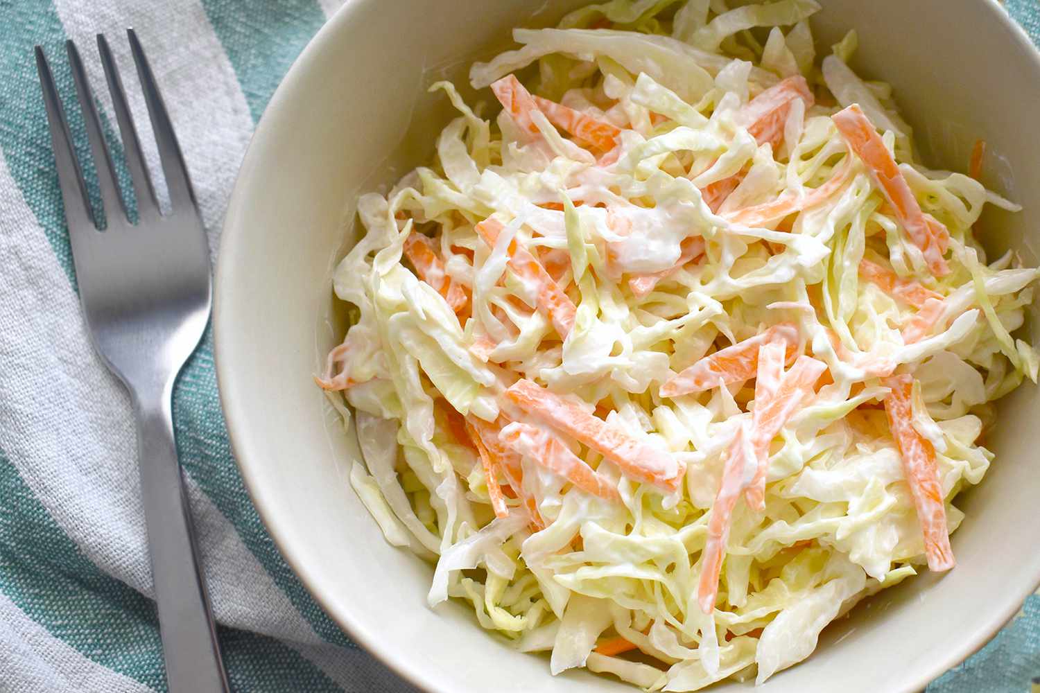 A bowl of coleslaw next to a fork