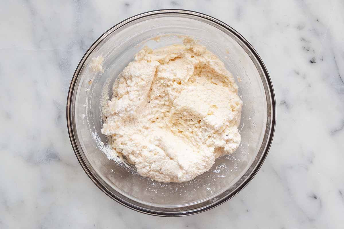 A small glass bowl with grated parmesan and ricotta inside.
