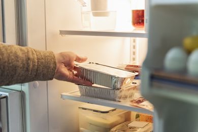 A hand reaching into a refrigerator to grab a takeout container