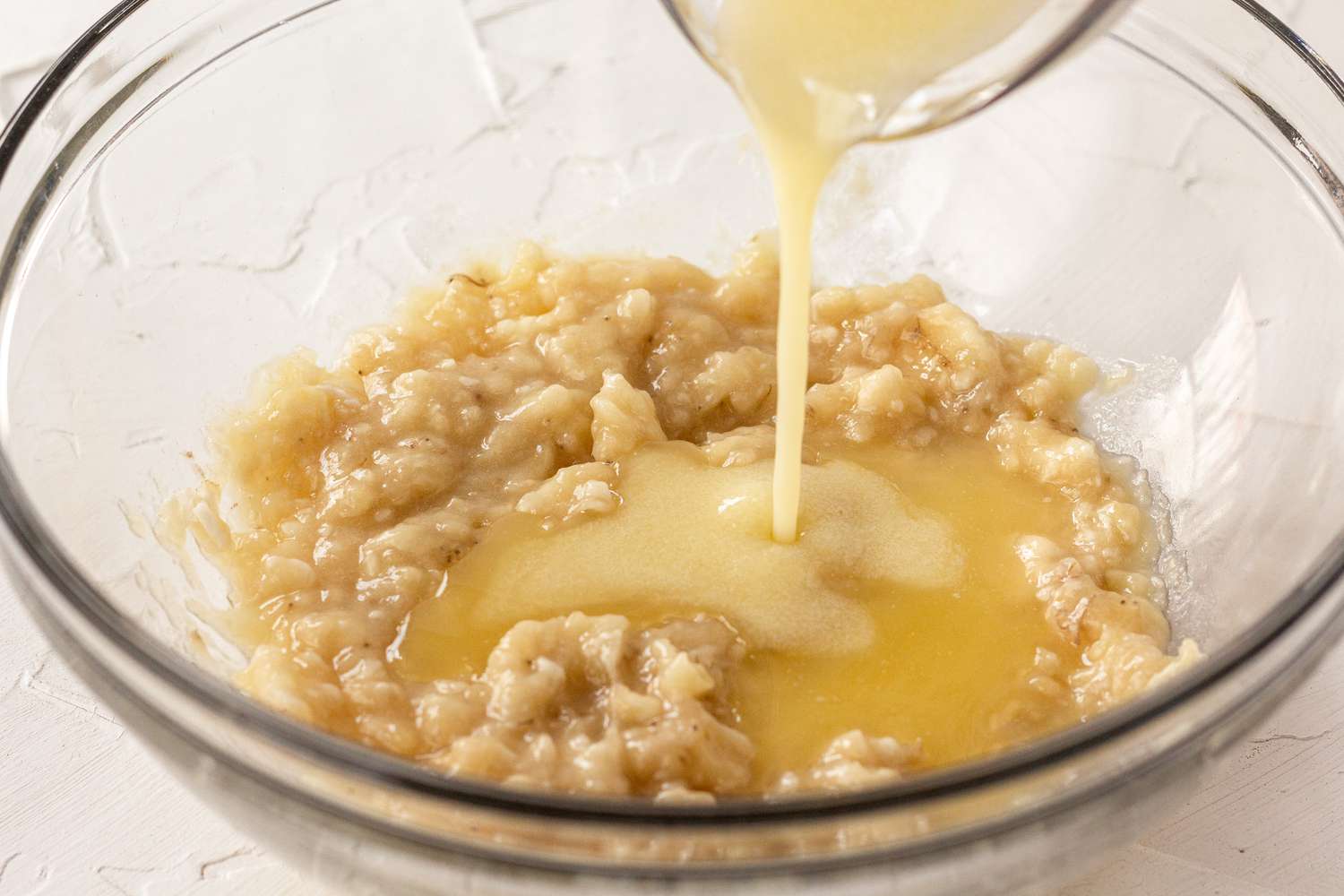 Melted butter added to a bowl of mashed bananas.