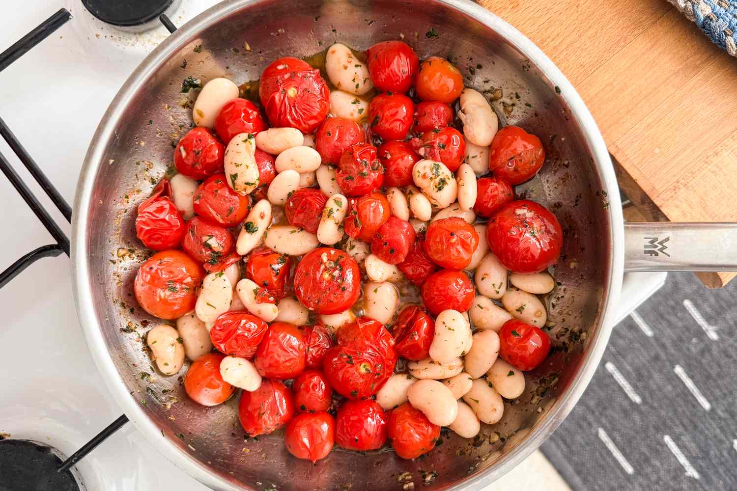 A skillet containing cooked cherry tomatoes and white beans with herbs on a stovetop for Crispy Halloumi With Tomatoes and White Beans