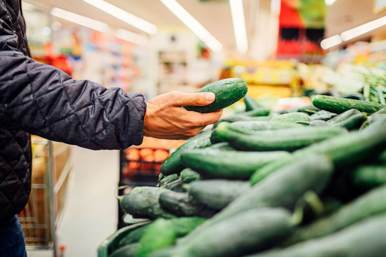 A person selects a cucumber from a display in a grocery store