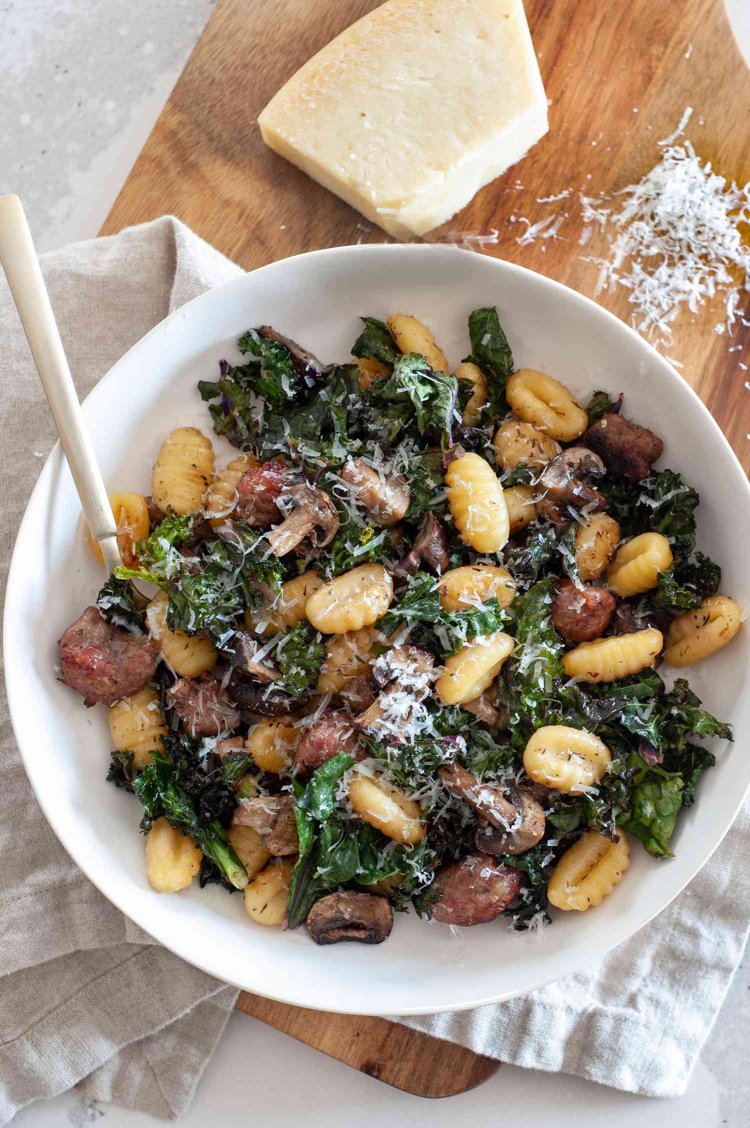 Sheet Pan Gnocchi With Mushrooms, Sausage, and Kale in a Bowl Next to a Block of Parmesan Cheese