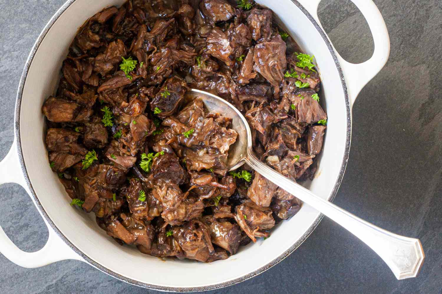 Overhead view of a dutch oven with braised oxtails inside for an oxtail recipe.