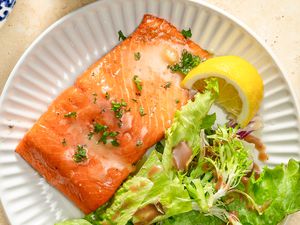 Closeup overhead shot of a roasted salmon fillet next to a green salad and a lemon slice on a plate