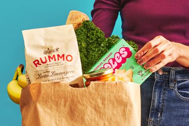 Paper bag of groceries, a woman's hand is pulling out a box of mac and cheese