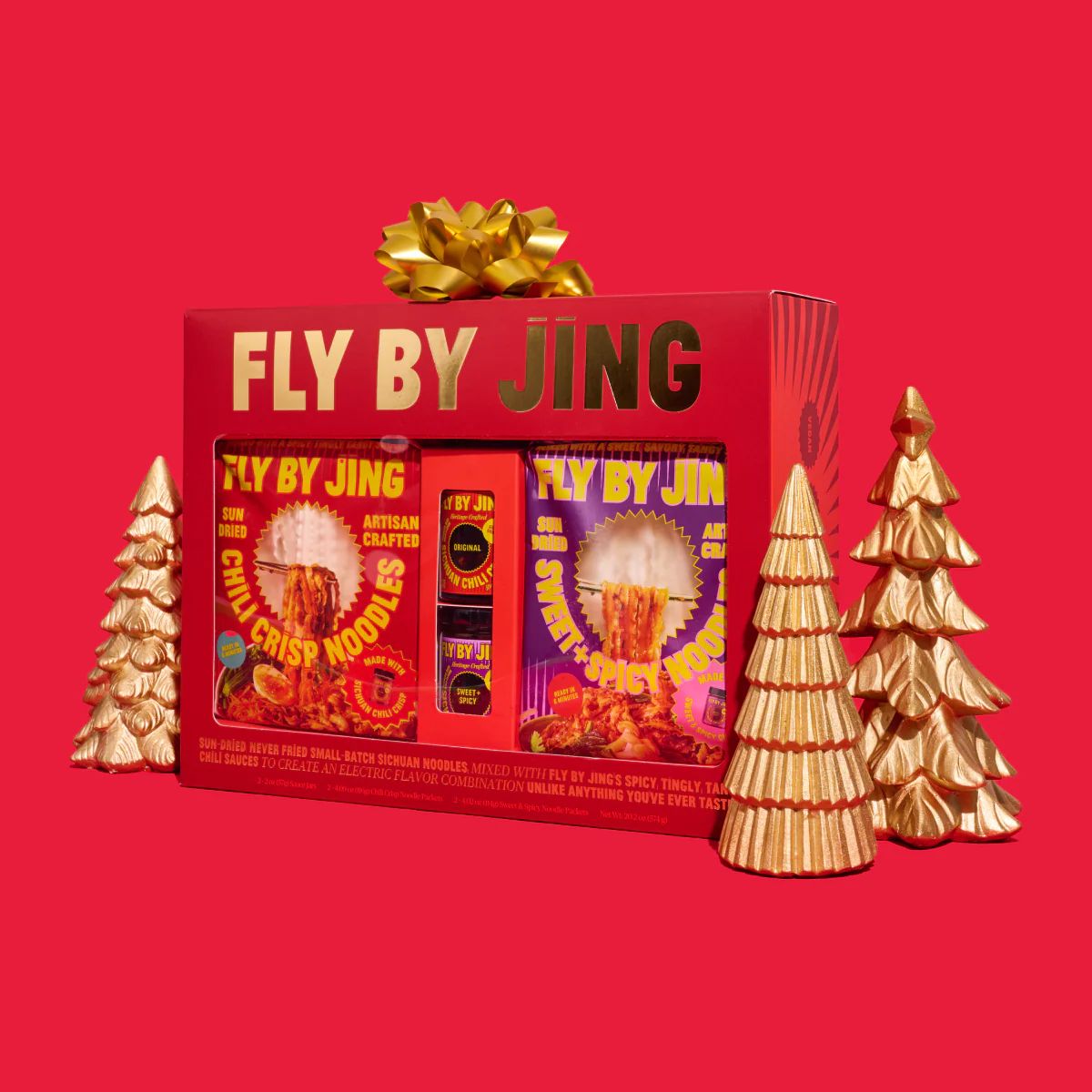 A gift box labeled Fly By Jing displayed with decorative Christmas trees containing various food items