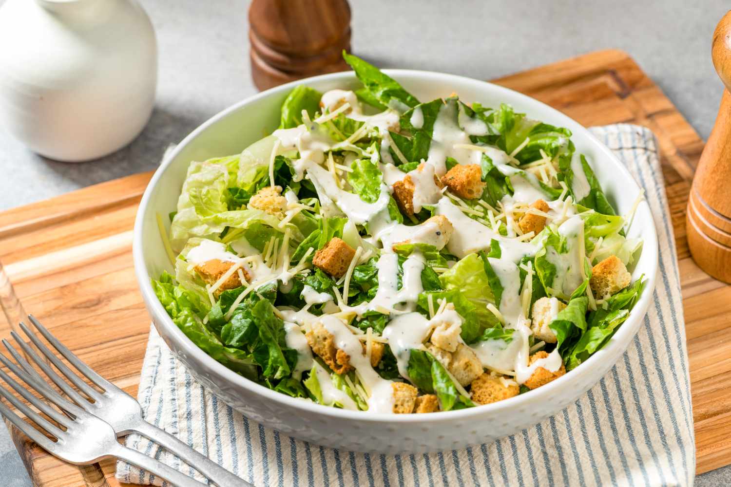 Caesar salad in a bowl with croutons and dressing on a striped towel on a wooden board