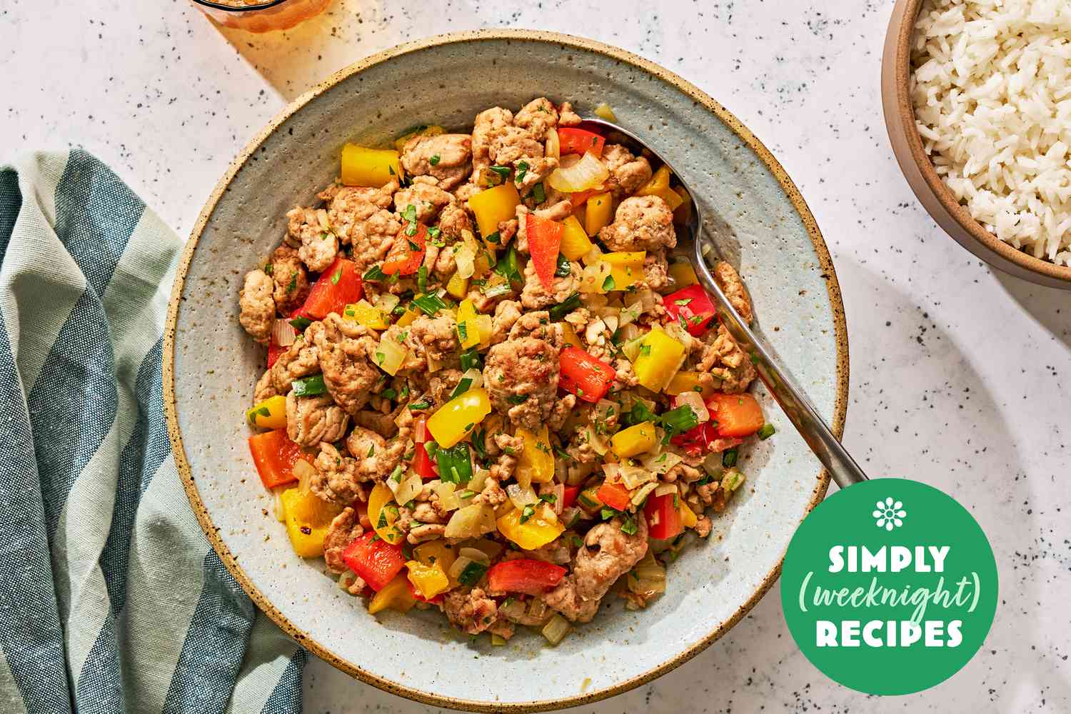 Ground turkey and peppers in a grey bowl with a spoon and white rice on the side in a brown bowl