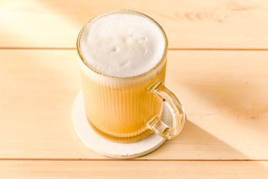 A mug of coffee with foam on top placed on a coaster on a wooden surface