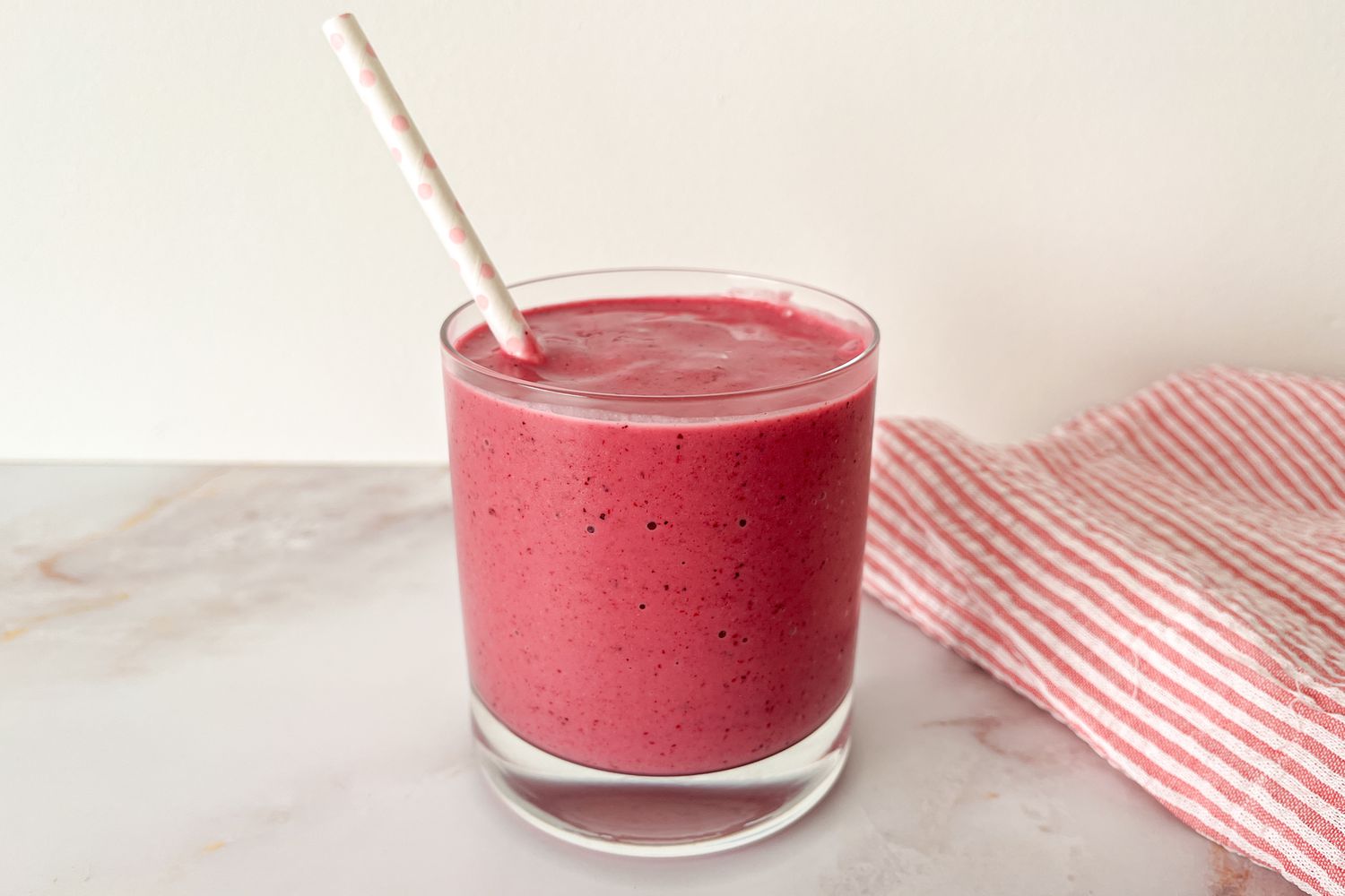 A short glass filled with a pink smoothie and a white paper straw with light pink polka dots